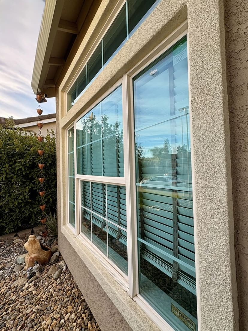Exterior view of a house window with shutters, surrounded by decorative stones and greenery.