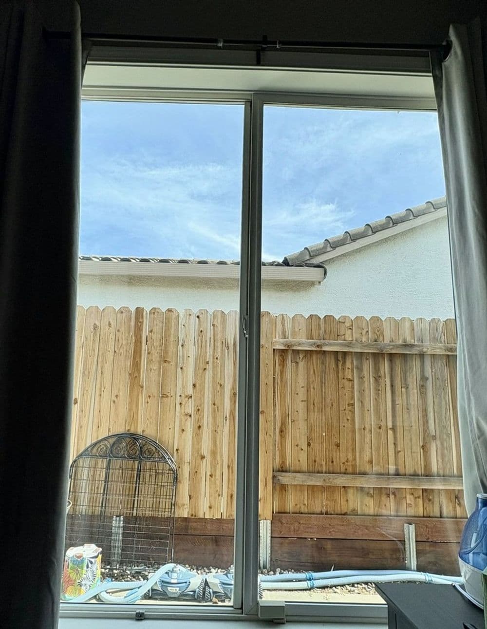 View through a window showing a wooden fence and blue sky with scattered clouds.