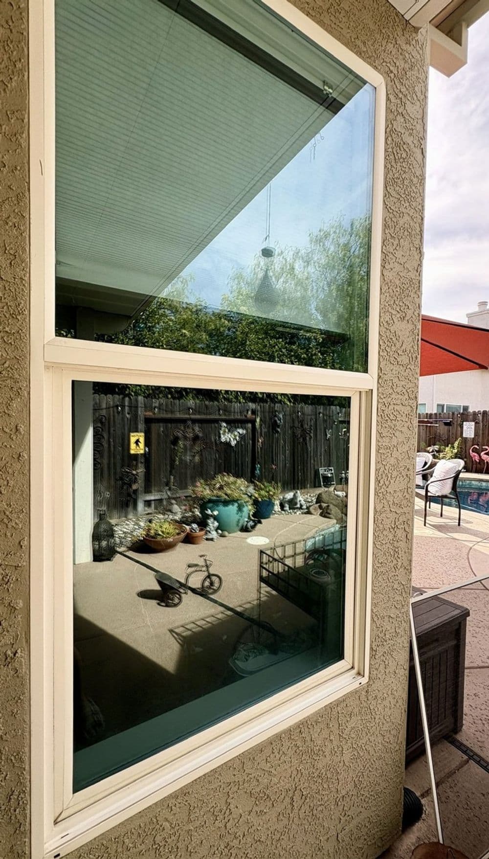 Window reflection showing outdoor garden and patio area with decorative plants and furniture.