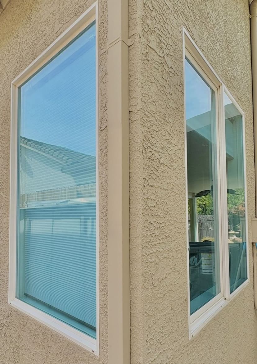 Two large windows on a textured beige wall, showcasing clear glass and horizontal blinds.