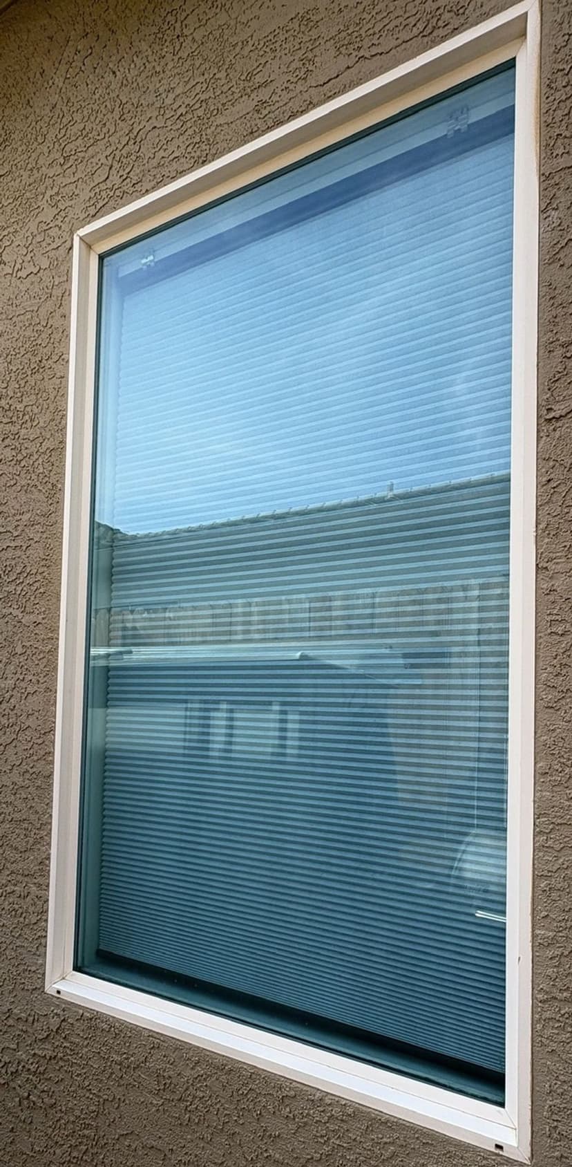 Window with horizontal blinds reflecting exterior buildings.