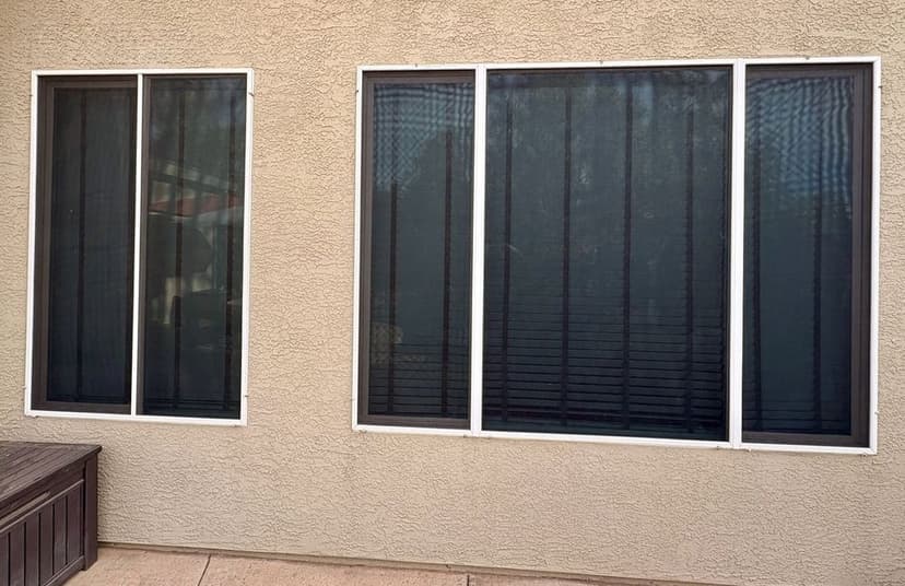 Modern home exterior featuring three windows with black mesh screens on a textured beige wall.