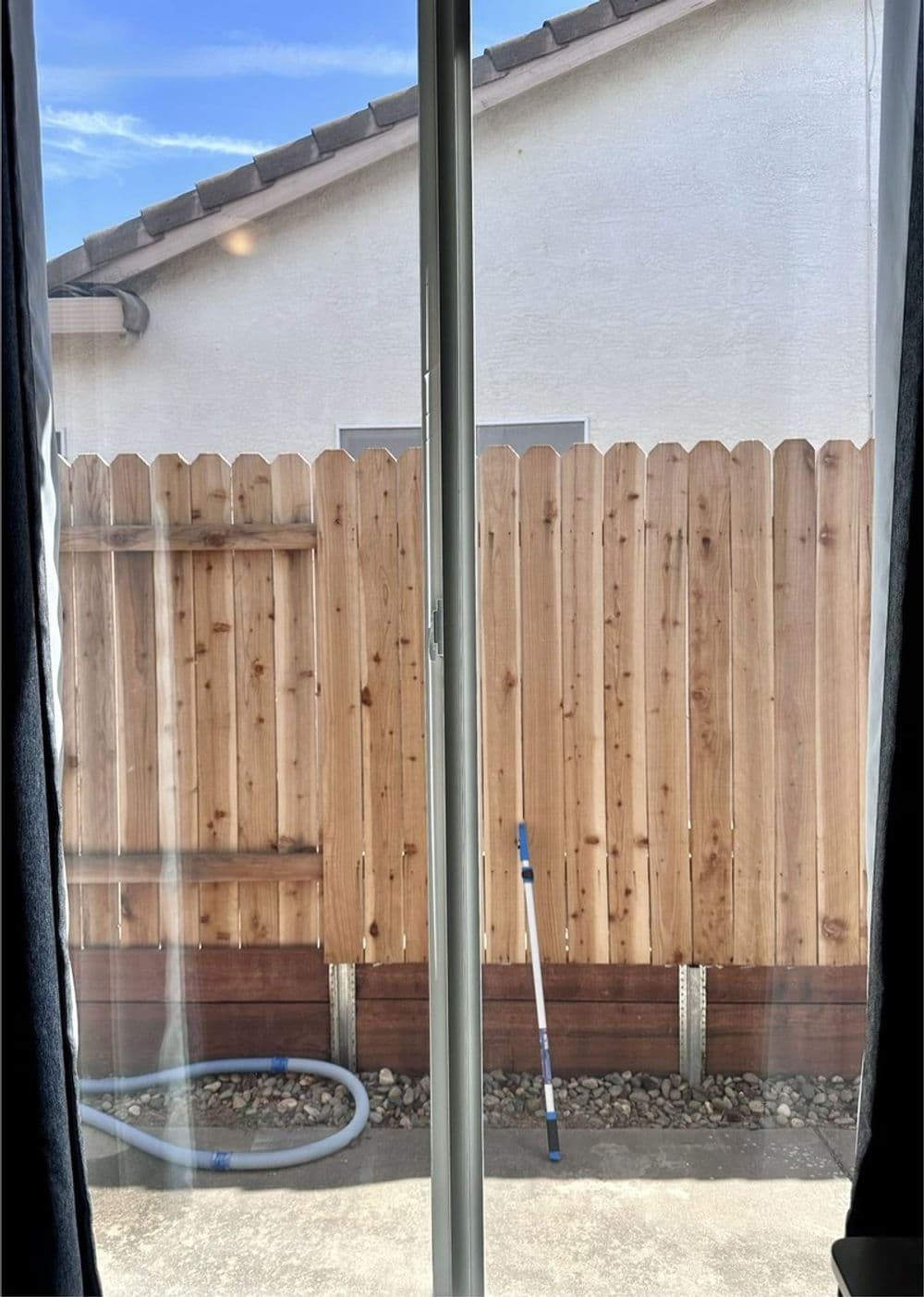 View through sliding glass door showing a wooden fence and garden tools outside.